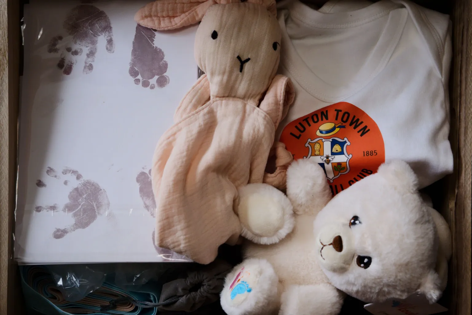 Laurence Cawley/BBC A memory box contains a white sheet with hand and foot prints, a pink rabbit comforter, a white teddy bear and a Luton Town FC T-shirt