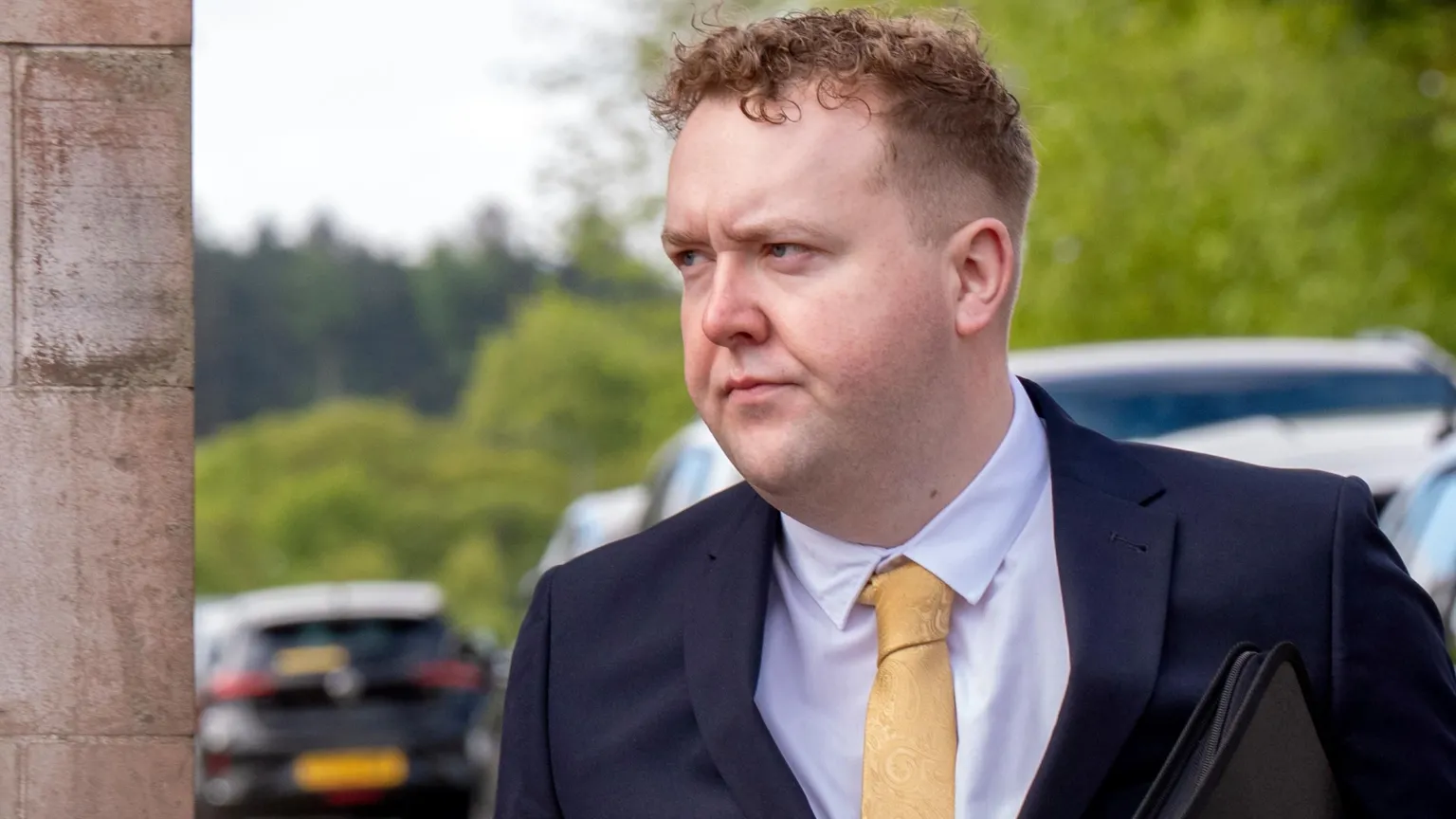  Jordan Linden arriving at court. He has short brown hair and is wearing a dark blue suit, pink shirt and yellow tie.