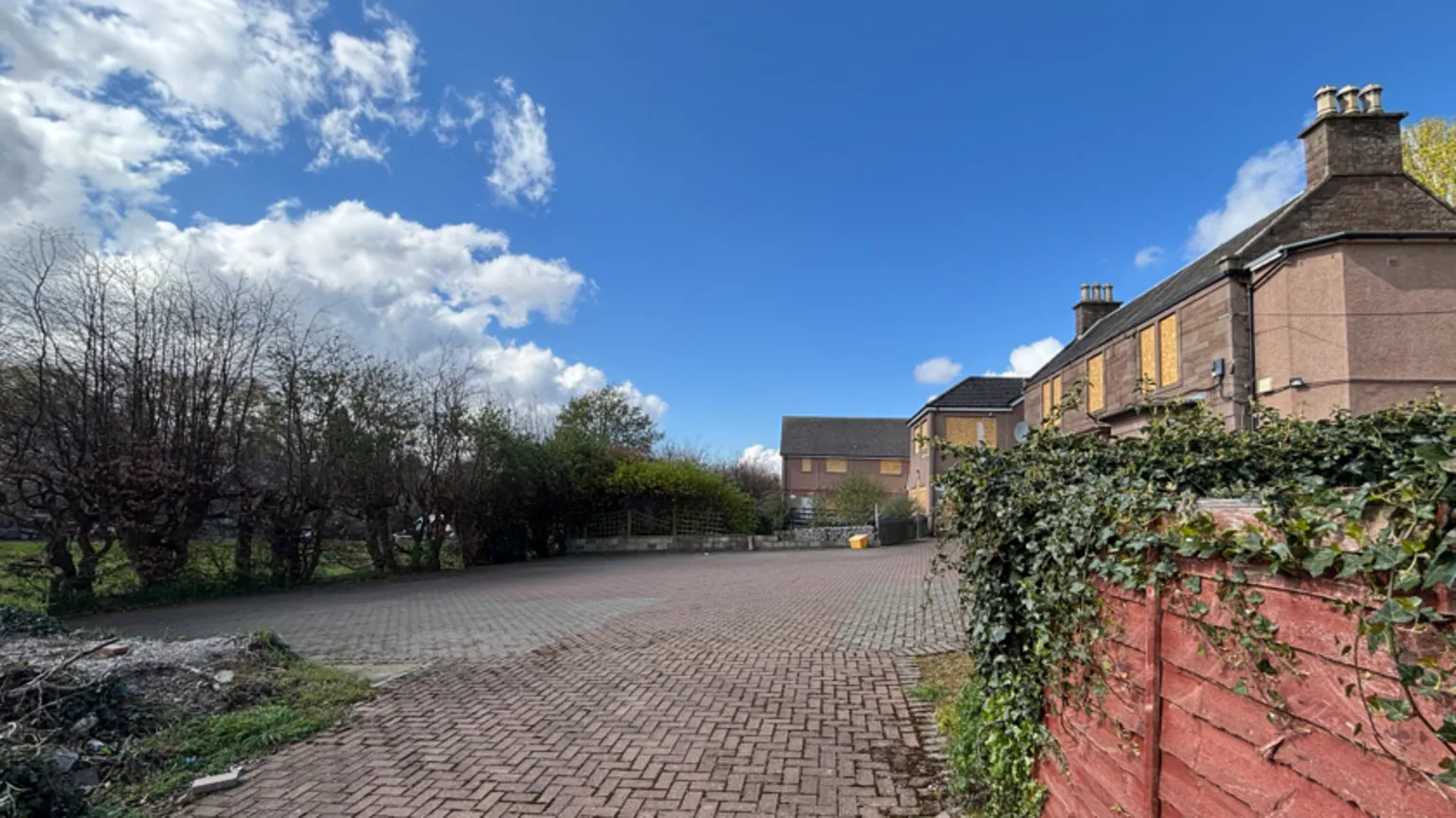 A large paved driveway leading to a large house with some trees in the distance