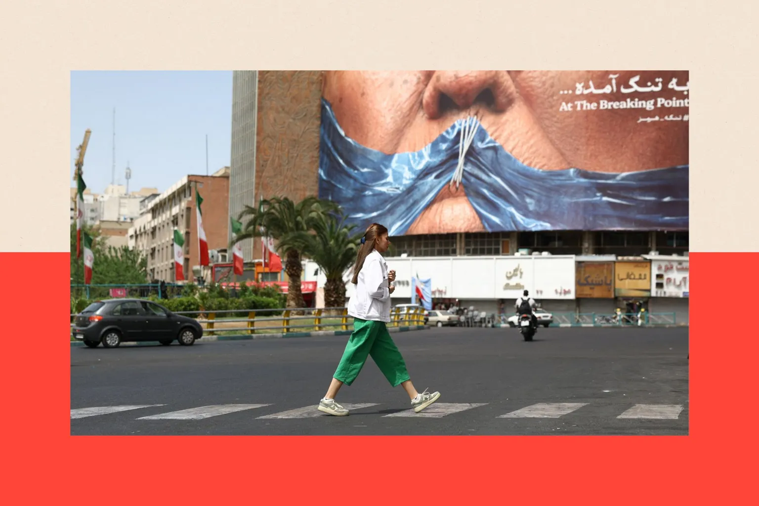A woman wearing a white shirt and green trousers walks in front of a billboard showing the Strait of Hormuz as a gag stitched across Trump's mouth