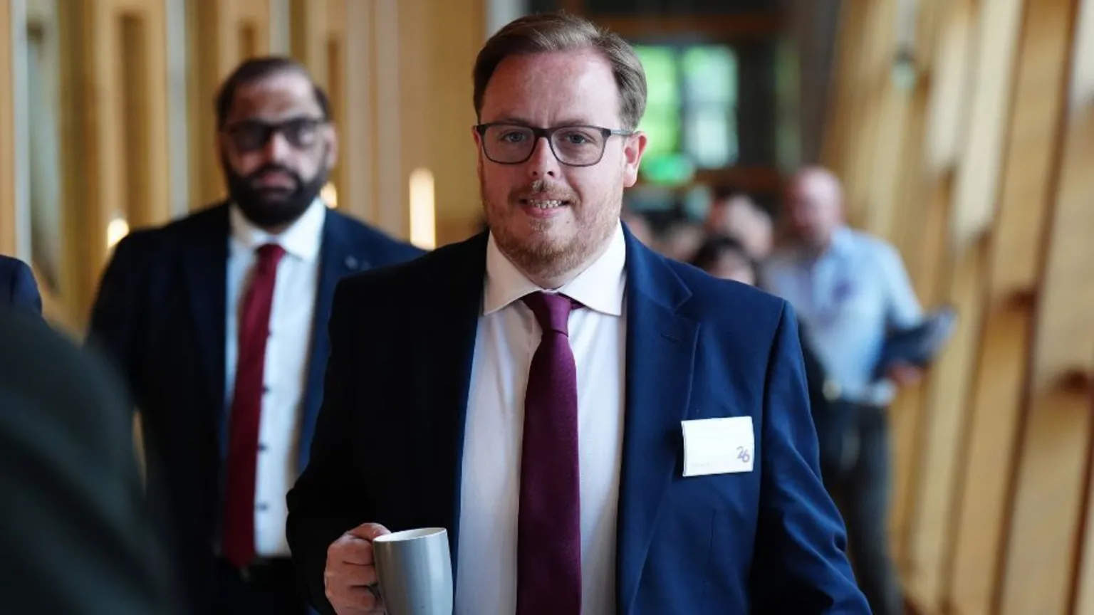 Thomas Kerr, who has fair hair and glasses, walks with a mug in his right hand