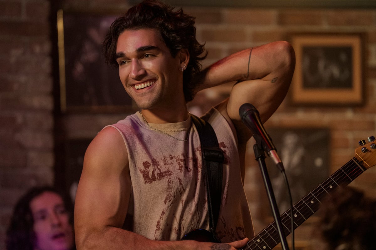 A man with very muscly arms wearing a singlet, and smiling.