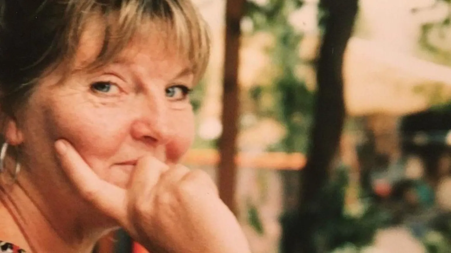 Armstrong family Light brown-haired woman, Gail Armstrong, is looking sideways at the camera with her hand on her face, smiling. The background is blurred.