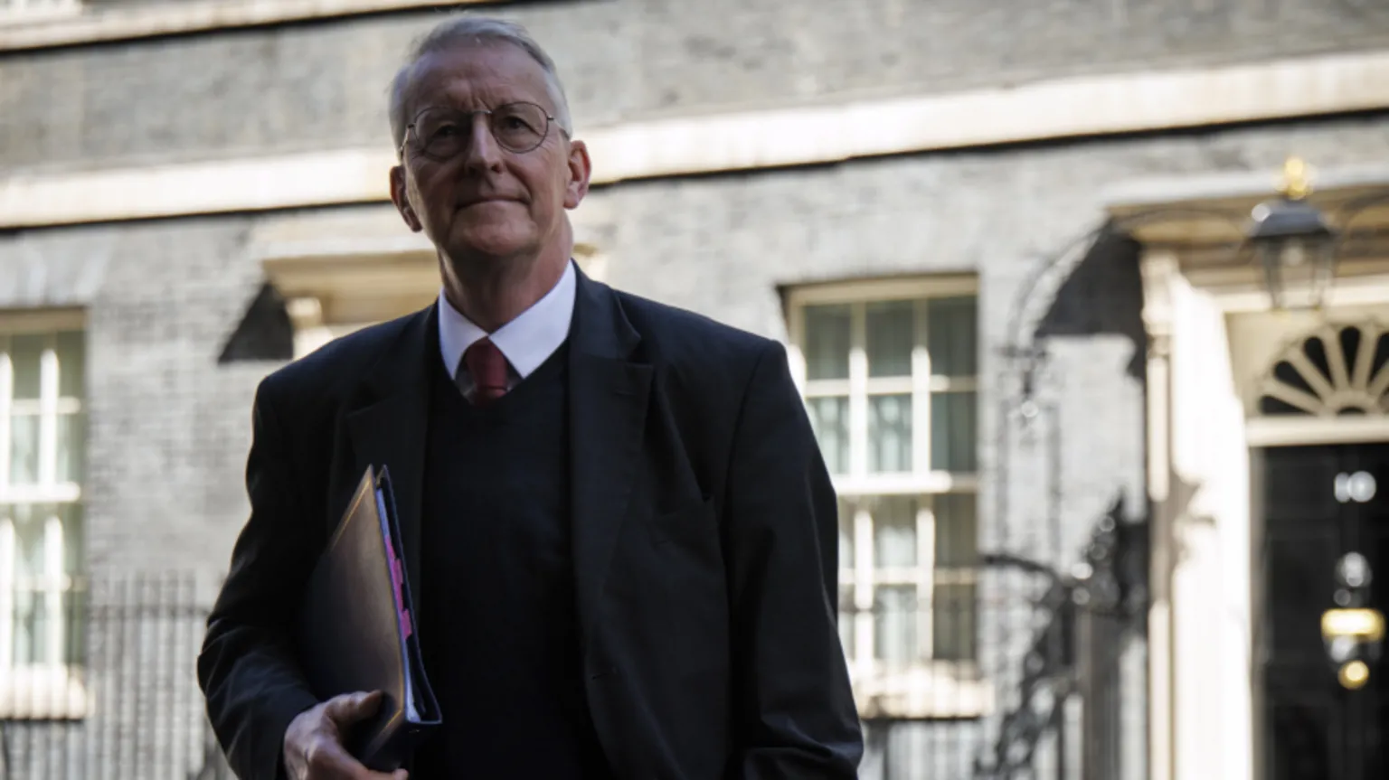 EPA The Secretary of State for Northern Ireland Hilary Benn is standing outside of 10 Downing Street. He is wearing a black blazer and jumper and is carrying a black jumper under his arm. 