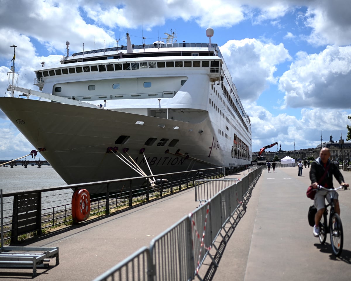 A man rides his bicycle past the Bahamas-registered cruise ship Ambition after passengers were confined following the outbreak of a gastrointestinal illness onboard, at the Bordeaux port in southwestern France.