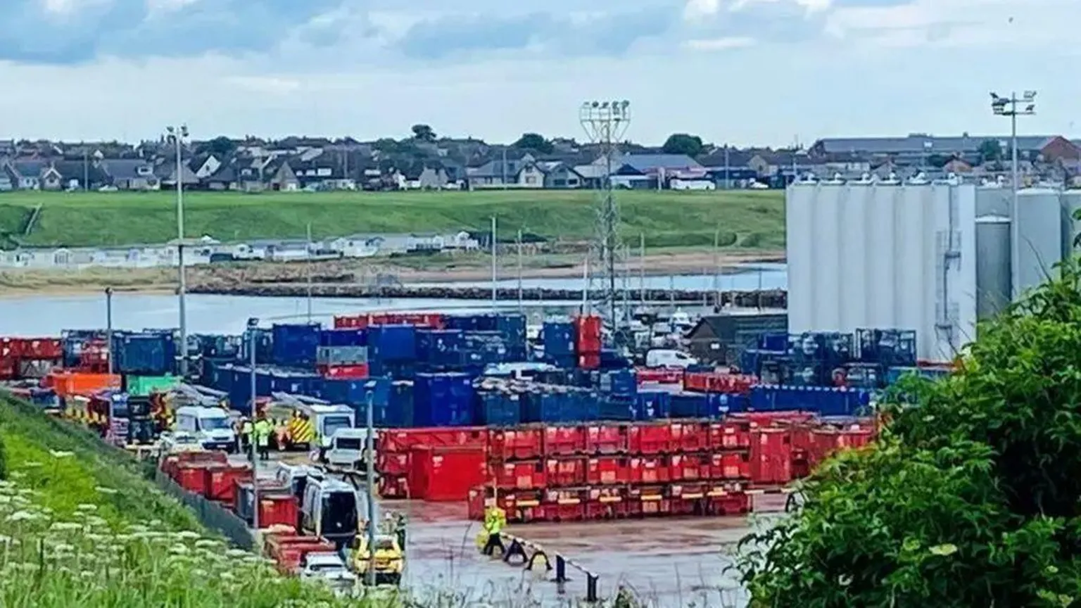 Emergency services at an industrial base, with sea water and then houses in the distance.
