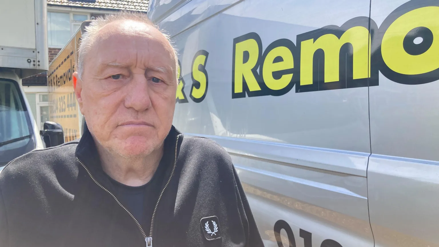 Mousumi Bakshi/BBC A man is looking concerned while standing next to a silver van with a yellow logo on it which says 