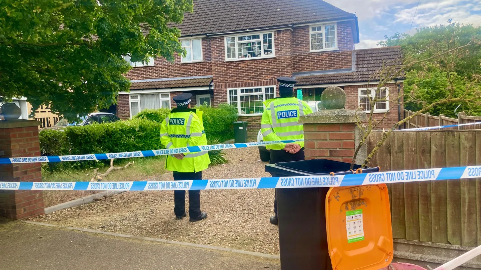 Mousumi Bakshi/BBC Blue and white police tape blocks a driveway of a house where two police officers are standing with their backs to the camera.