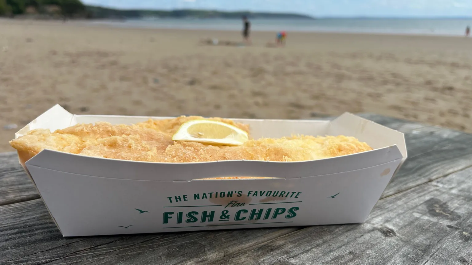 Cod, with a slice of lemon, in fish and chips tray on bench looking out at the sea
