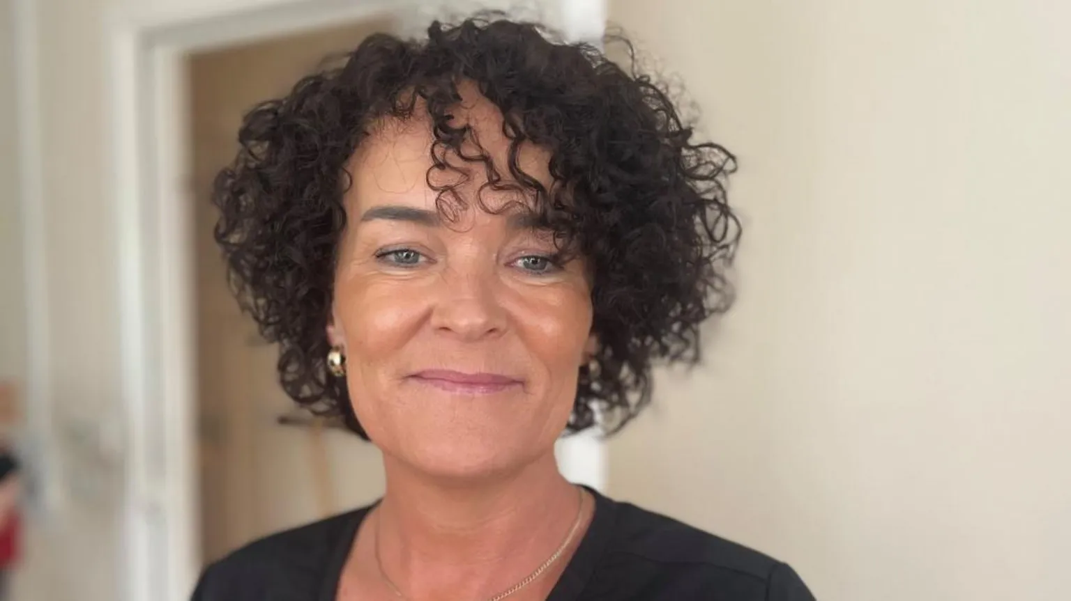 Bronagh is smiling at the camera. She has tight black curly hair and is wearing a black top.