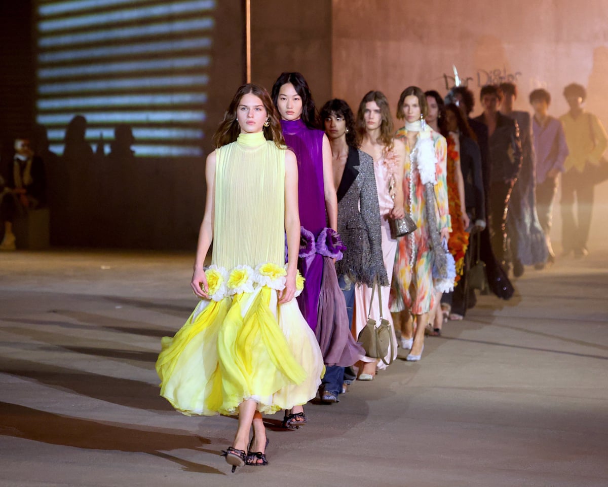 Models in dresses in a line, one behind the other, on the catwalk.