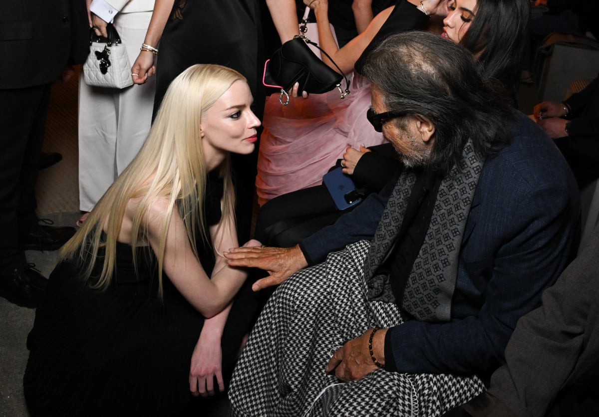 Taylor-Joy crouches listening to Pacino, seated, while. he touches her lightly on the arm