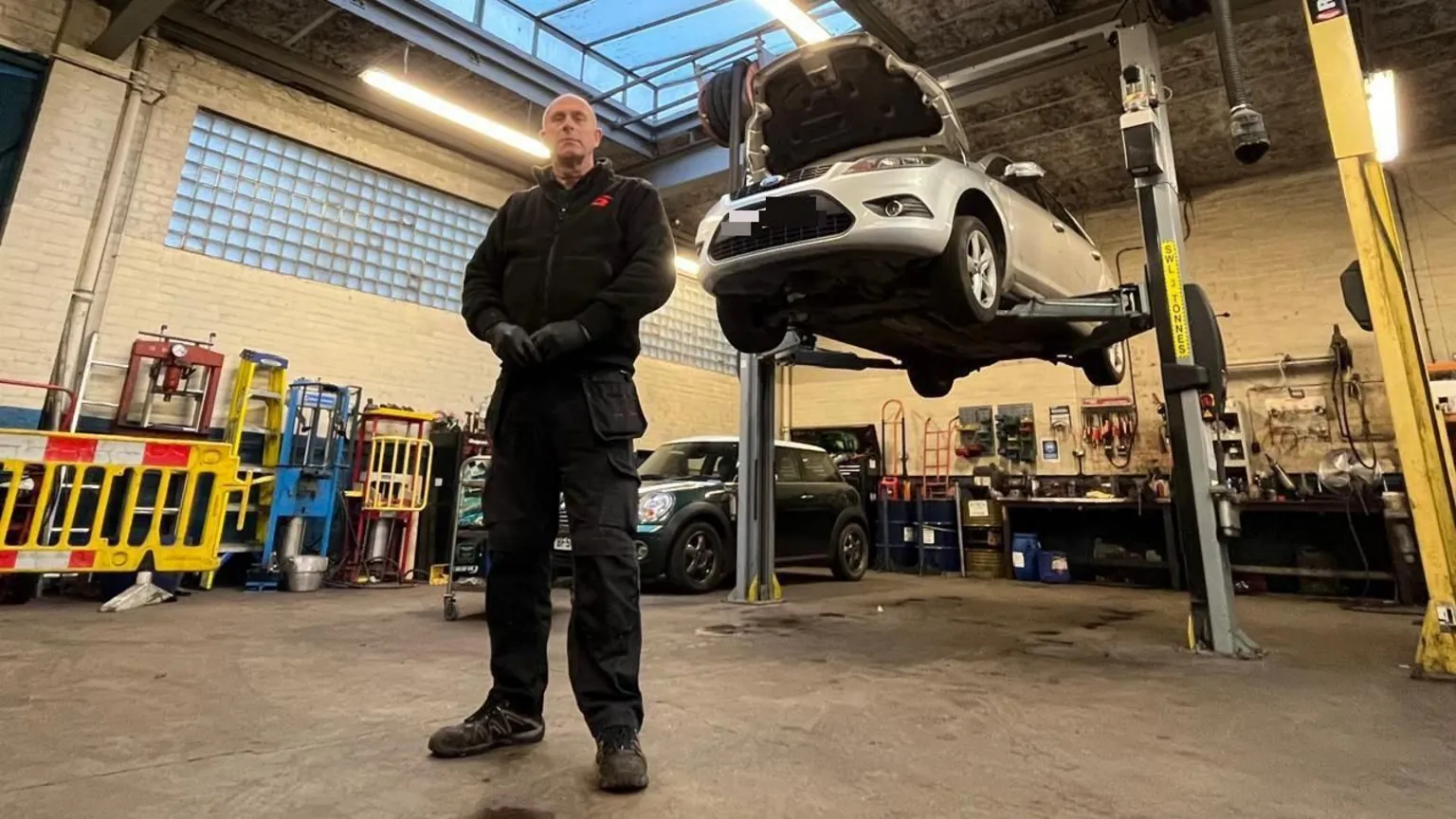 Mechanic Mick Hampshire standing in front of a suspended car in his garage in Netherfield.