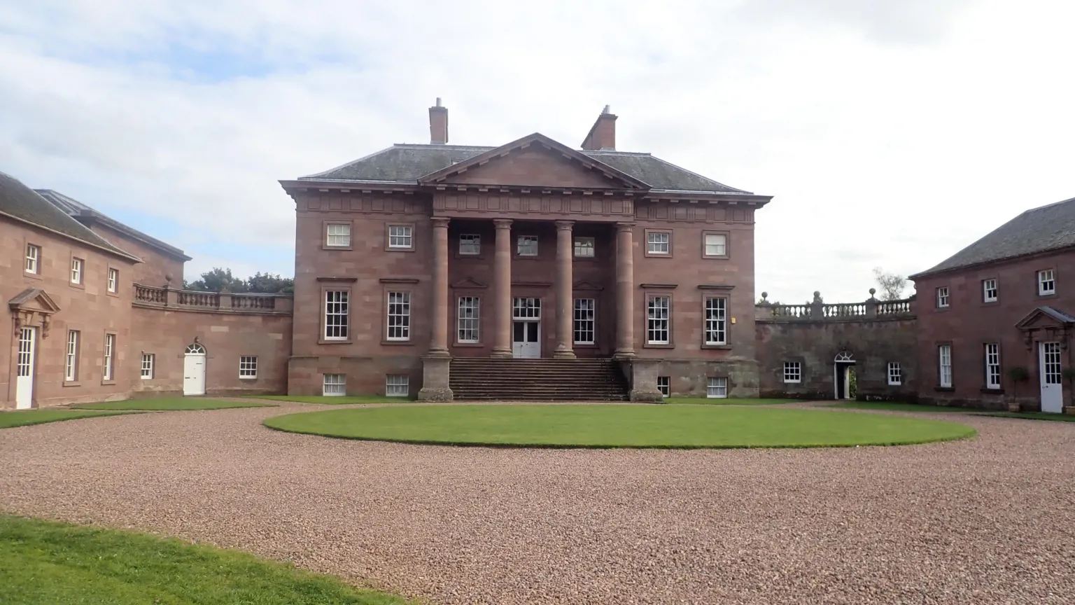 Eirian Evans An 18th Century country house in sandstone with pillars at its main entrance around a circular courtyard with a round lawn and red gravel path around it.