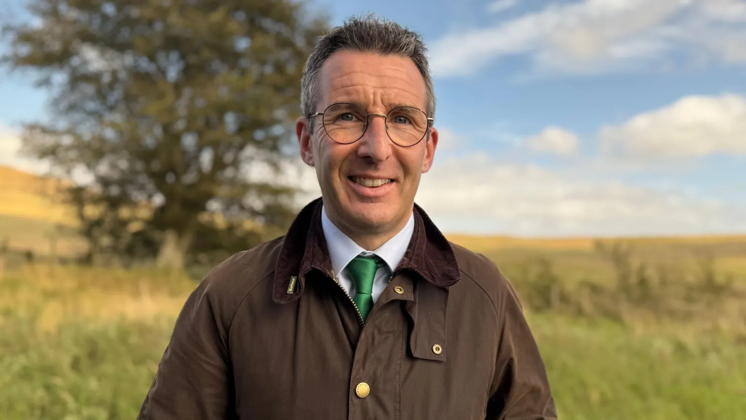 Andrew Muir, a man with dark hair, wearing a brown jacket, white shirt and green tie.