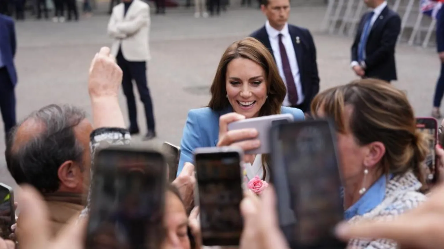 Mobile phones are held in the air to take a picture of the Princess of Wales as she smiles greeting crowds, dressed in a pale blue blazer