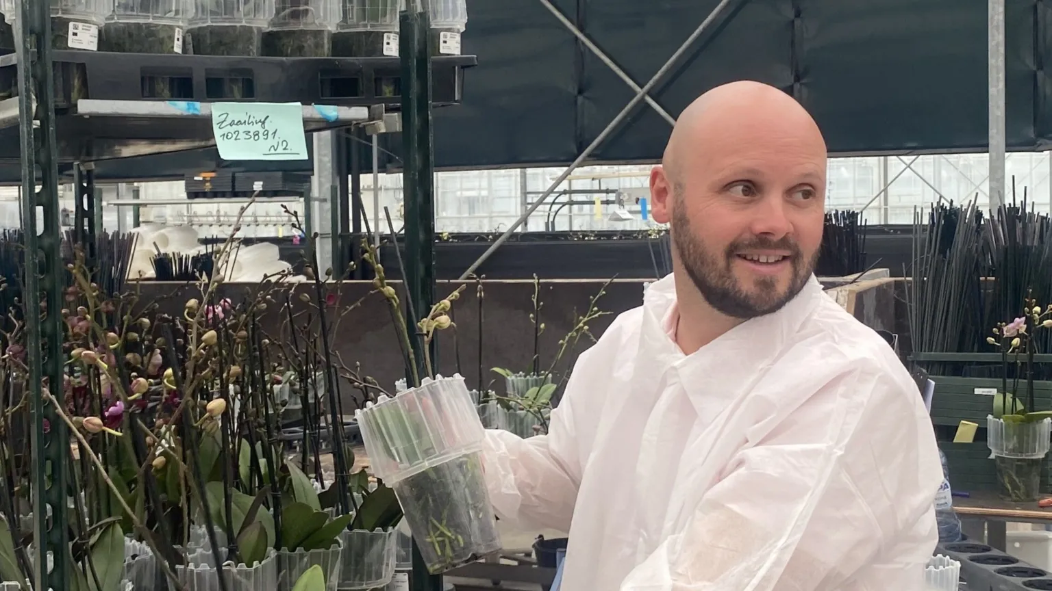 Stefan Kuiper wears a protective white suit and looks out of shot. Behind him are shelves of orchid plants. 