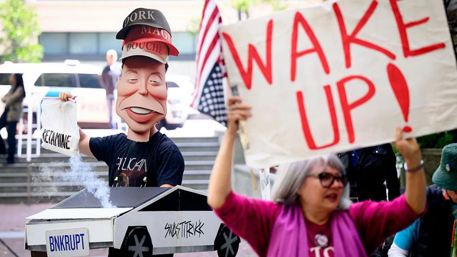 A model of Elon Musk wearing three hats which say 
