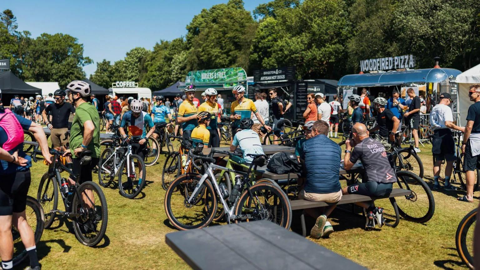 Red On Sports A large group of cyclists gathered around tables in the sunshine with mobile food trucks behind them