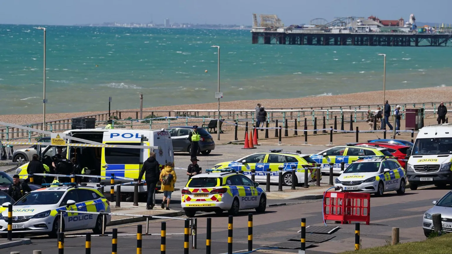  Various police vehicles in a car park on Brighton seafront. Brighton Palace Pier and a choppy blue sea are in the background.