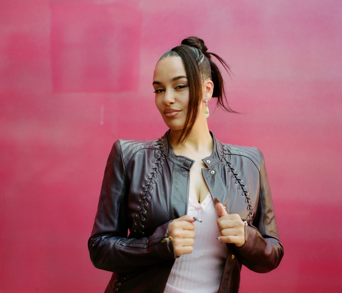 Jorja Smith poses in a black leather jacket against a crimson-coloured wall
