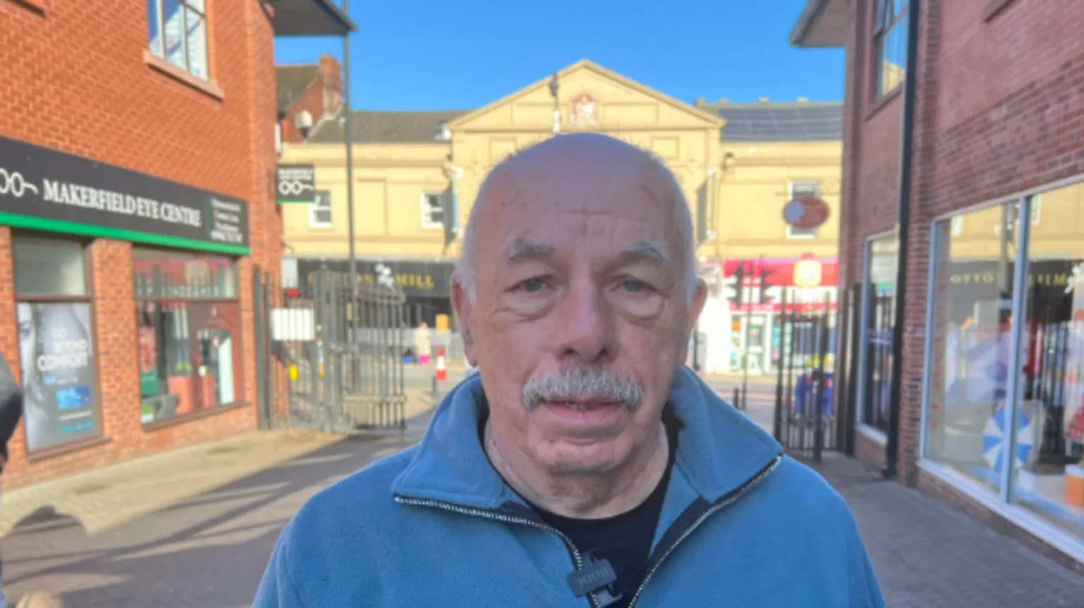 Stan Crook wears a blue jacket. He is looking at the camera. He has a moustache. 