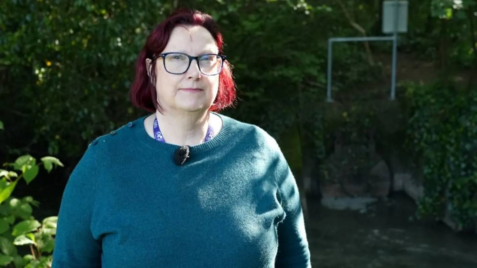 A woman with red hair and glasses wearing a green jumper