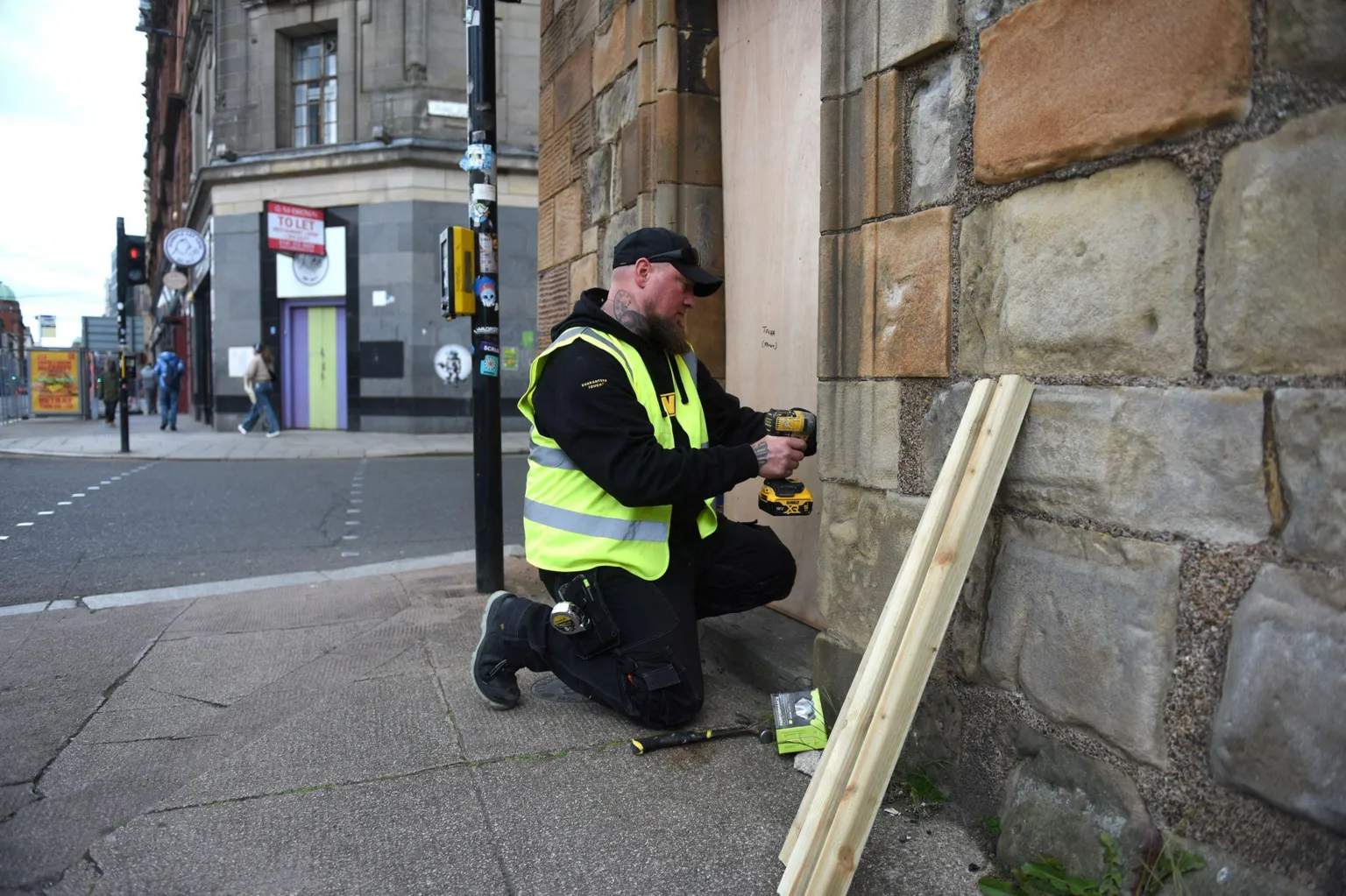James Chapelard A workman, wearing black clothing and a high-viz vest, boards up the entrance to Glasgow's historic Mercat Cross. He also has a a ginger beard and a neck tattoo and is wearing a black baseball cap.