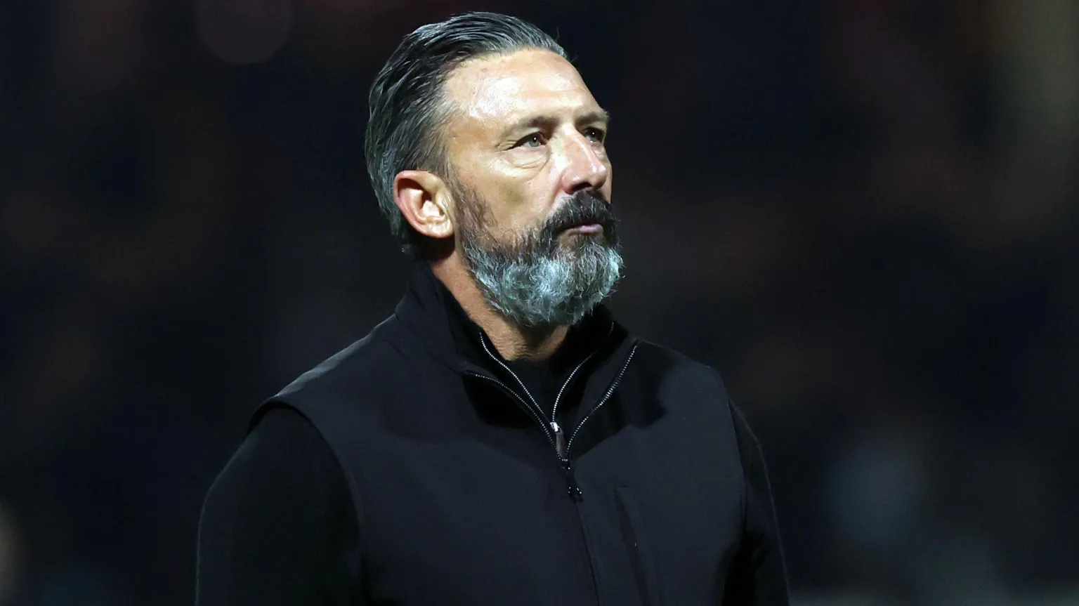  Hearts manager Derek McInnes, who has dark slick-backed hair, stares off to his left against a black background. He is wearing a black jacket and has a black, greying beard.