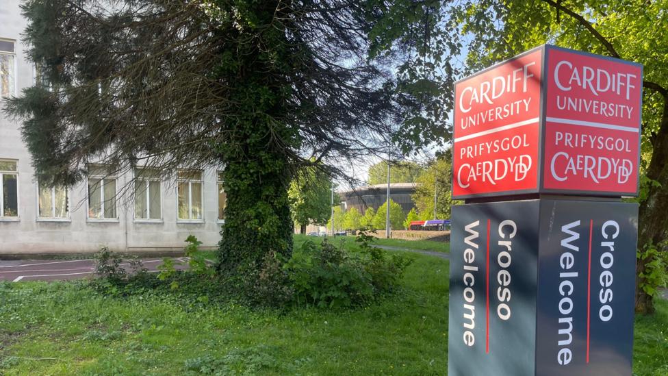Mae arwydd yn nodi “Cardiff University / Prifysgol Caerdydd”, gyda “Croeso / Welcome” oddi tano.