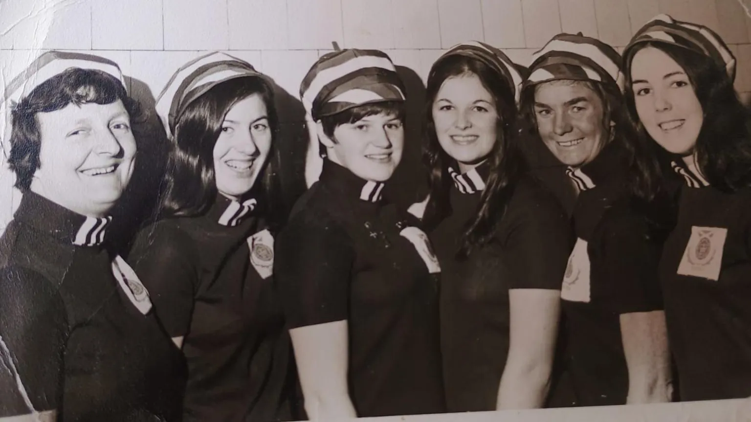 Anne Kane Mary and her synchronised swimming team standing in a row smiling at the camera. They are wearing dark coloured uniforms and stripy hats. 