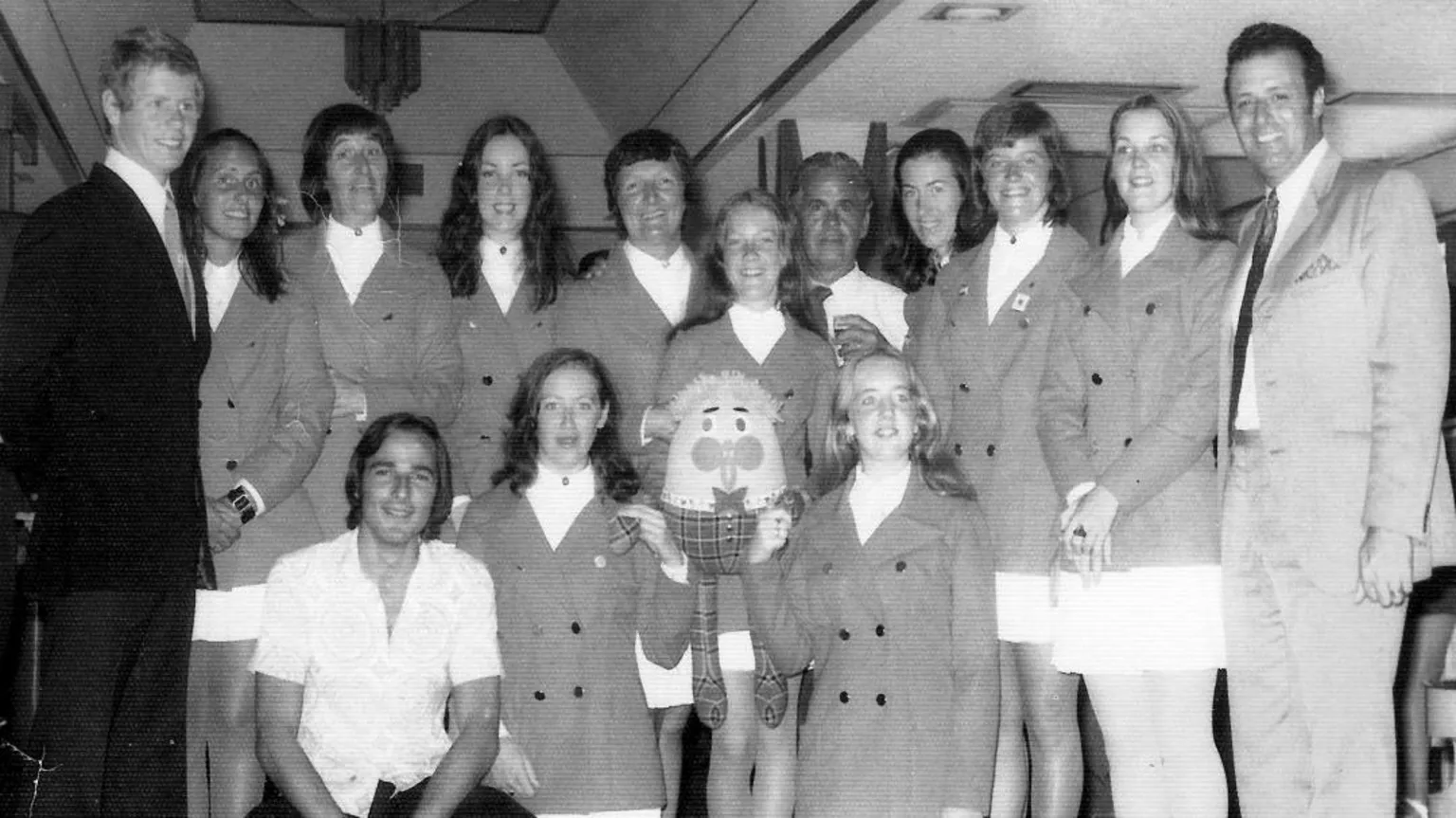 Kenneth Black Mary and her synchronised swimming team standing in a row smiling at the camera. They are wearing dark coloured blazers and white skirts.