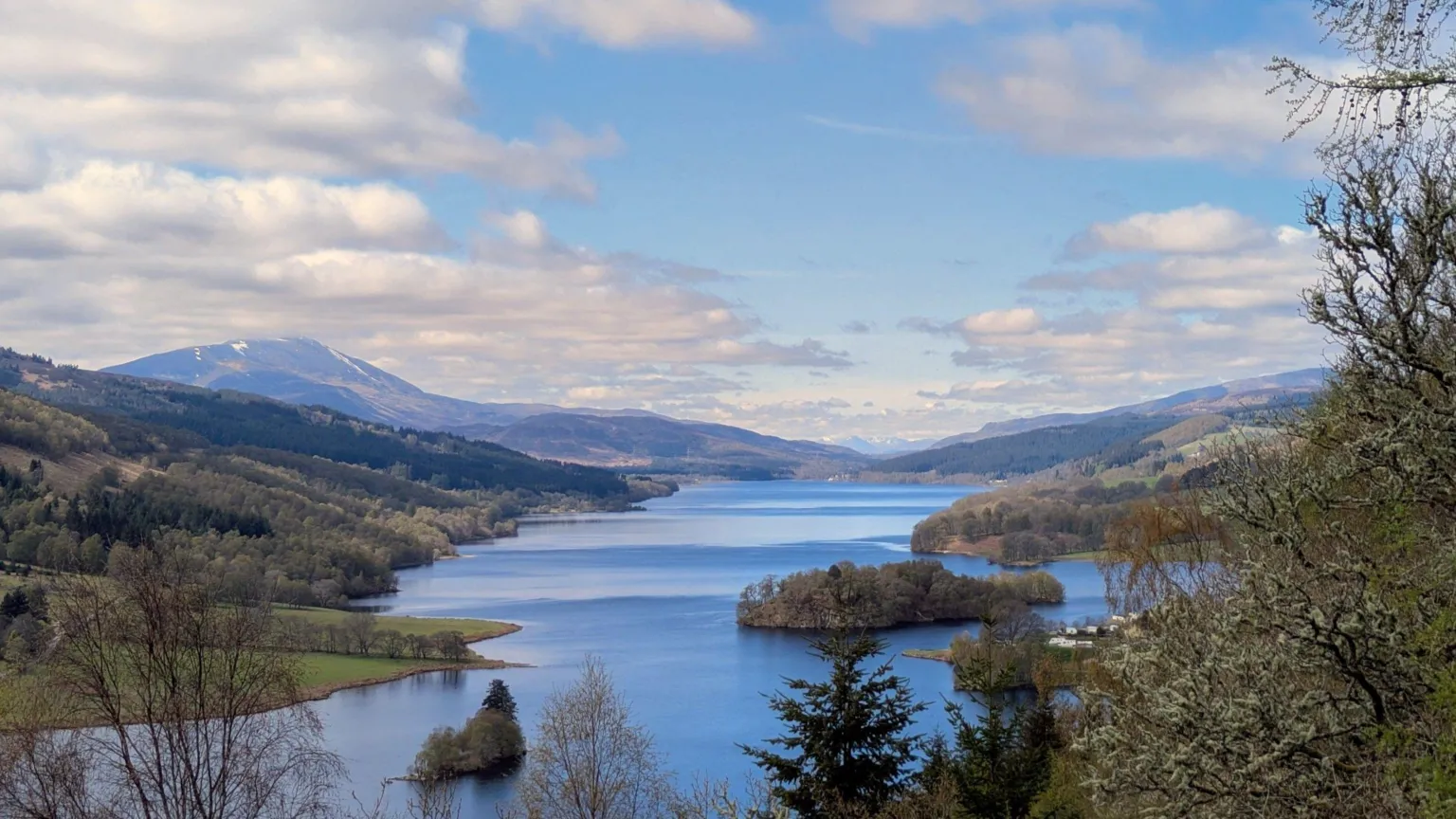 Ryan Gearing A view along a lake with hills and trees either side under a cloudy blue side.