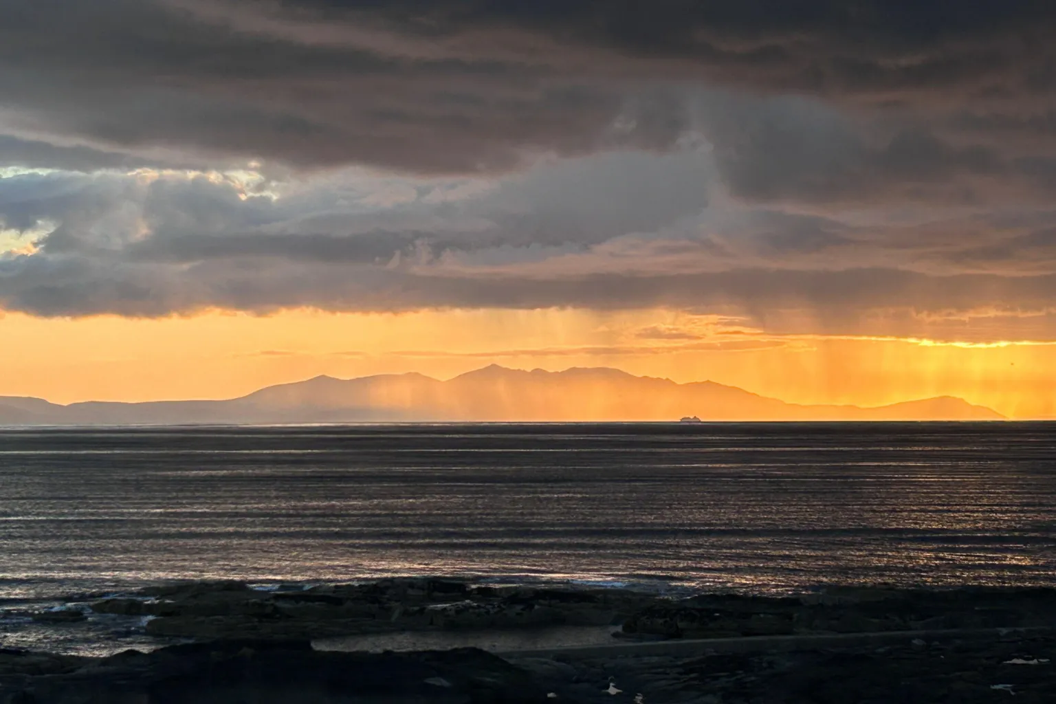 David Smith A ferry in the far distance, silhouetted against hills, under an orange sunset sky.