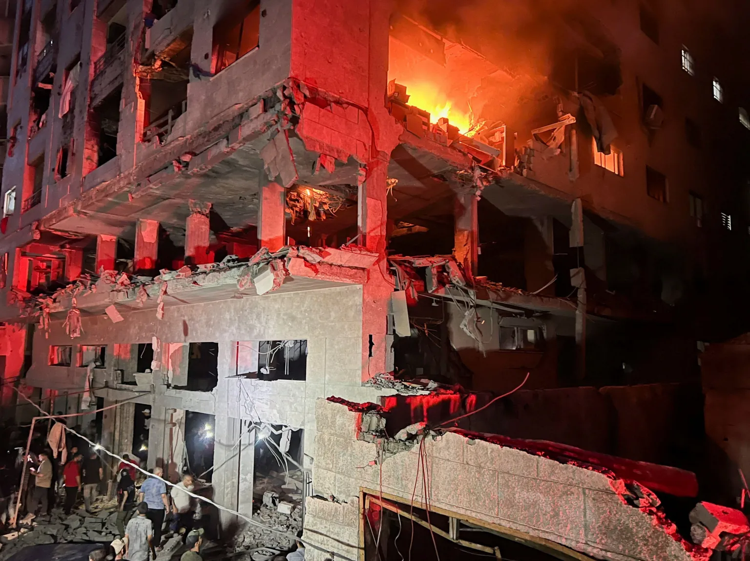  A fire burns in a residential building after Israeli shelling. People can be seen milling about below.