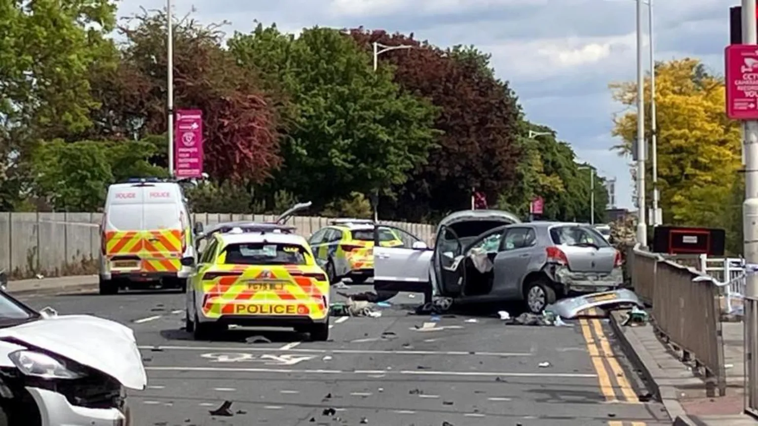 Several police vehicles can be seen parked on the road at the scene of the crash. Three cars can be seen with substantial damage.