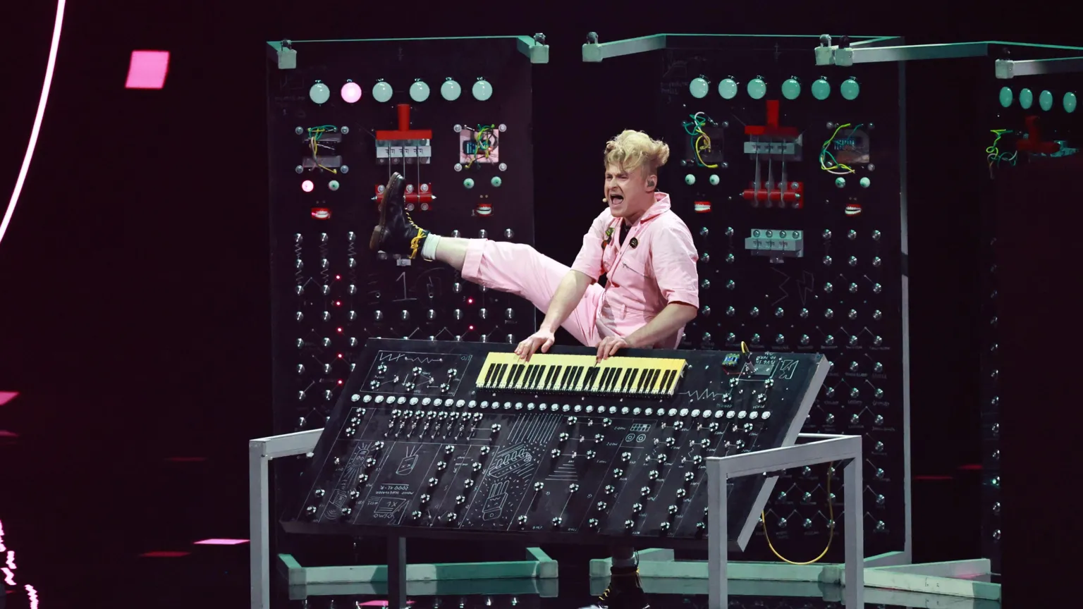 Sam Battle kicks his right leg into the air while playing a keyboard.
