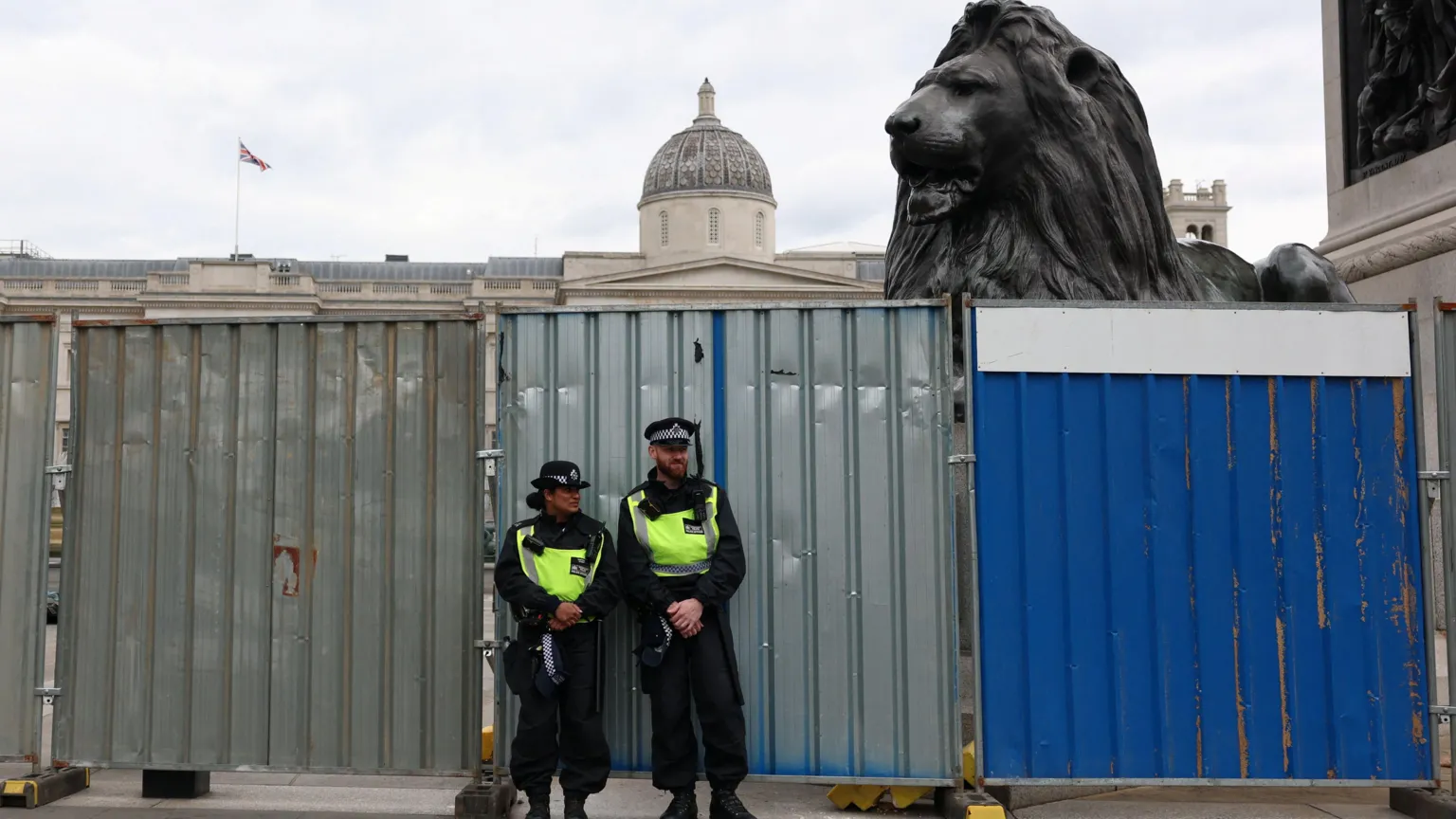  Two officers in front of a high metal barrier with one of the lions of Nelson's Column peering over the top.