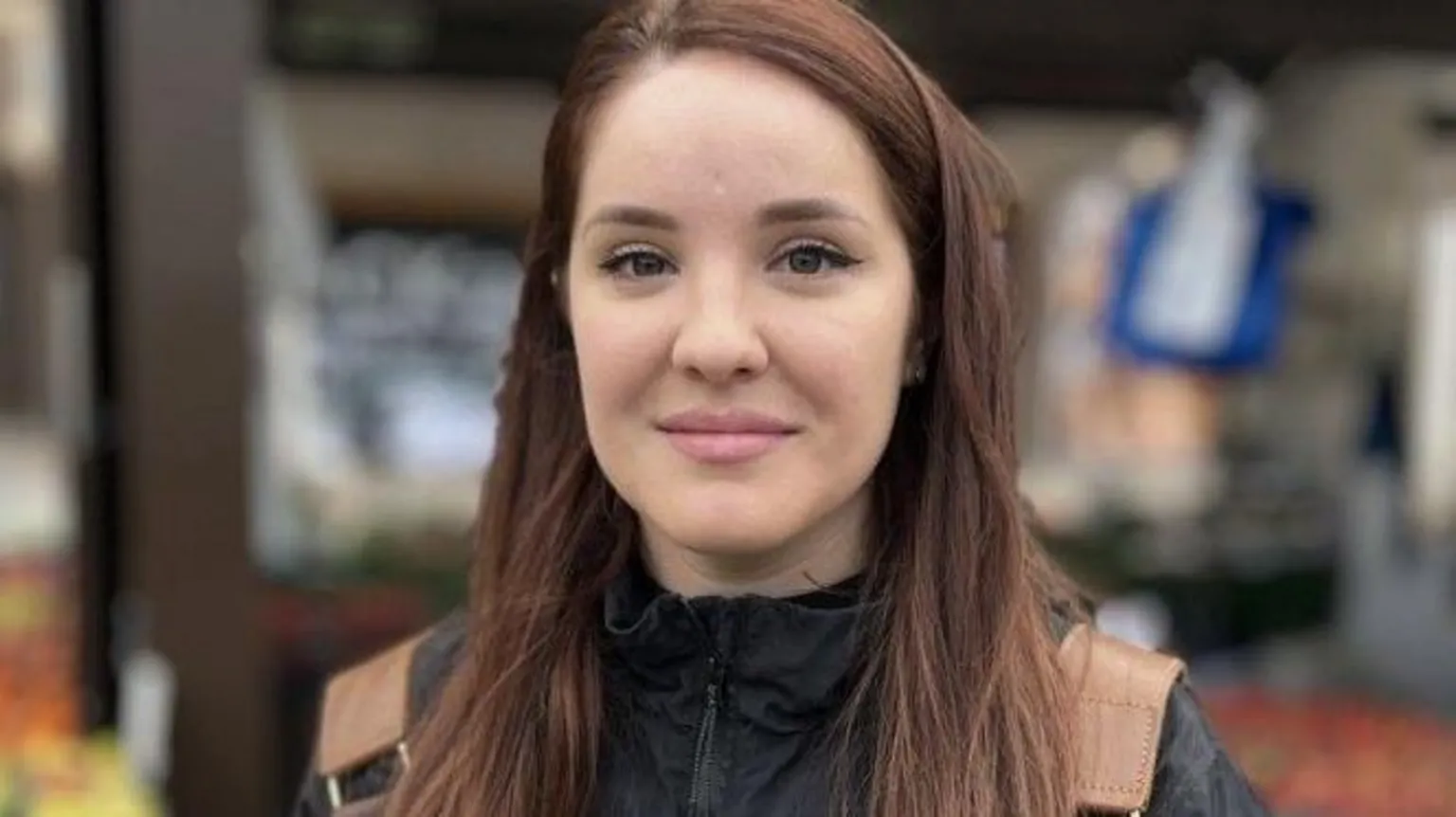 Martin Giles/BBC Maria Agachi smiles at the camera as she is photographed at a market. She is wearing a black rain jacket and brown backpack. She has long brown hair. 
