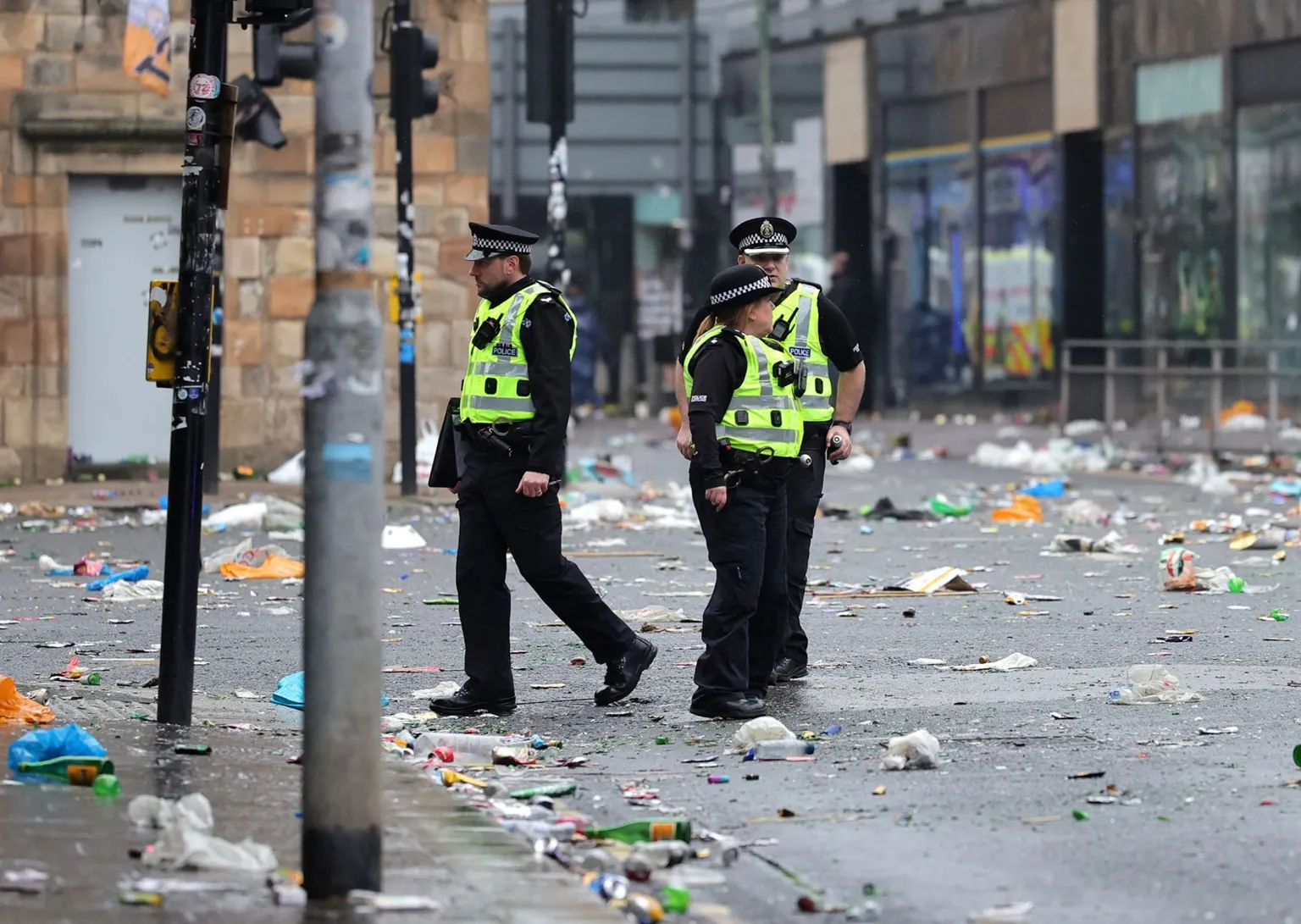 Police Scotland officers walk along a city street covered in litter and debris following large crowds gathering in Glasgow.
