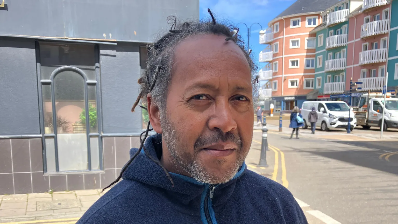 An image of a man standing near Aberystwyh promenade - dreadlocked hair, wearing a dark blue fleece 