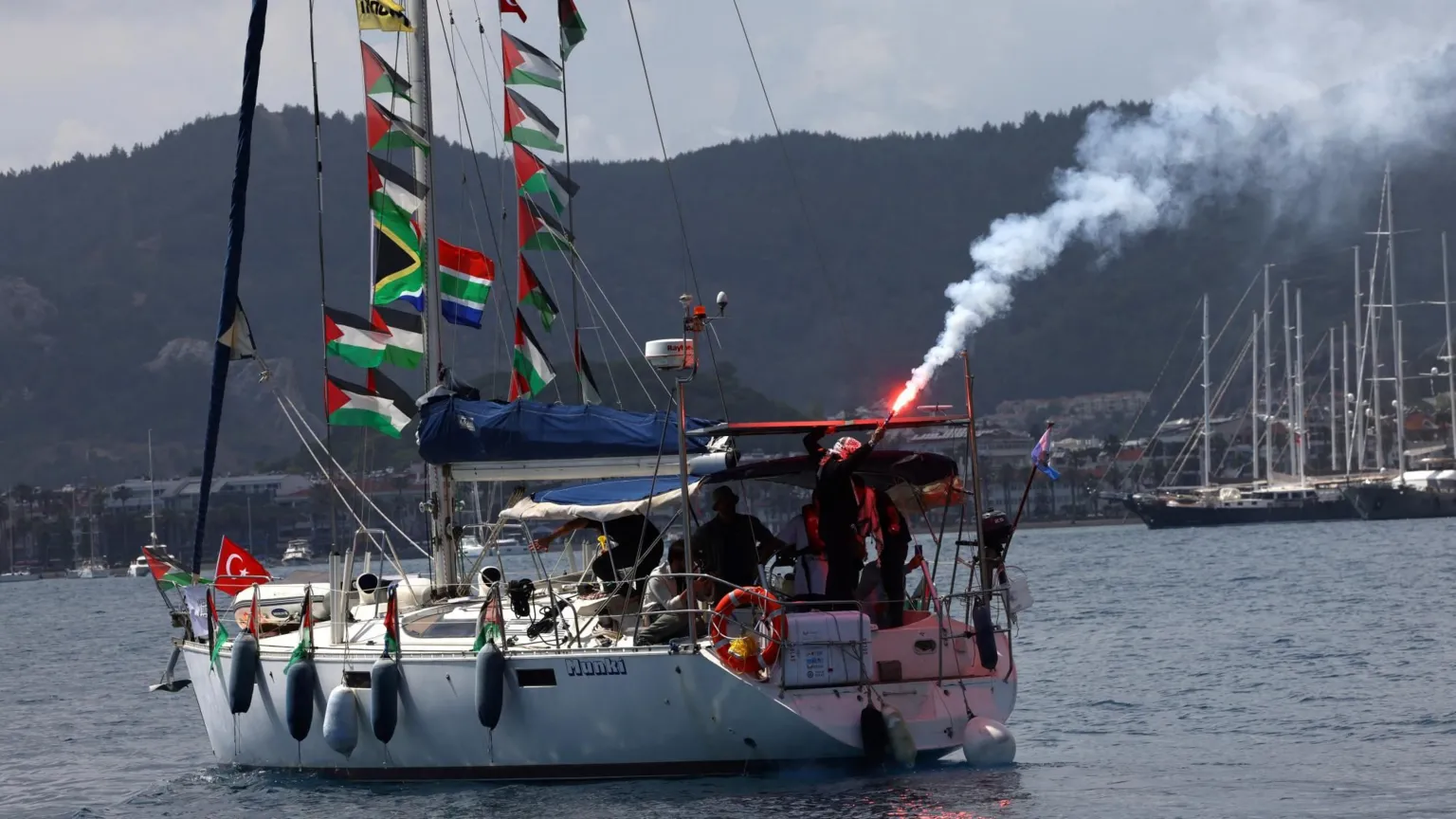 Activists on board a sailboat taking part in the Global Sumud Flotilla light flares as they depart from the port of Marmaris, southern Turkey (14 May 2026)