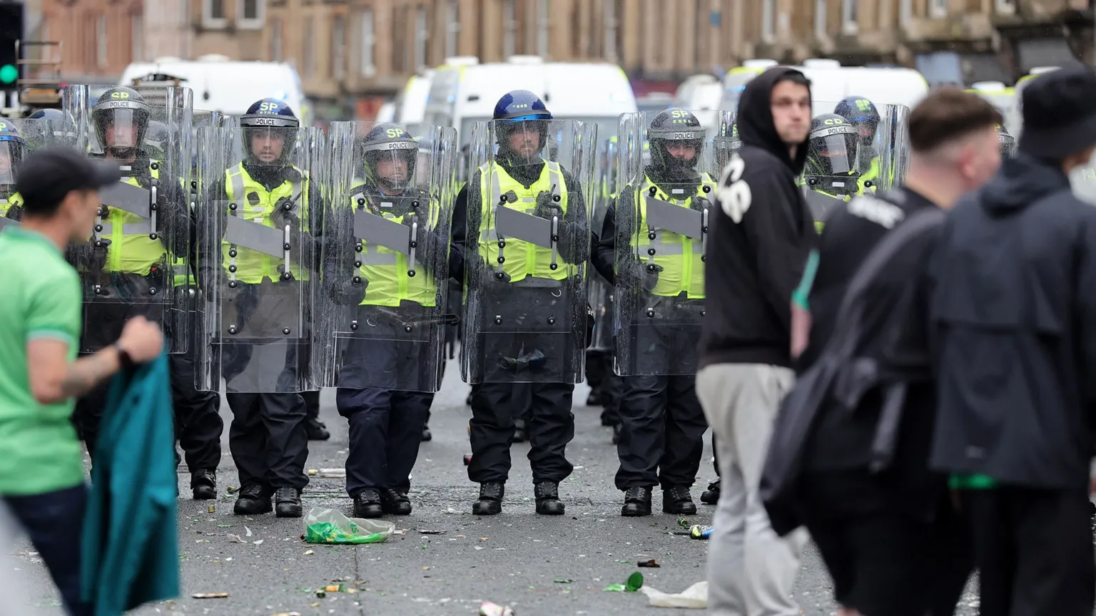  A line of Police Scotland officers in riot gear holding shields as they advance along a city street, with debris scattered on the ground and people in the foreground.