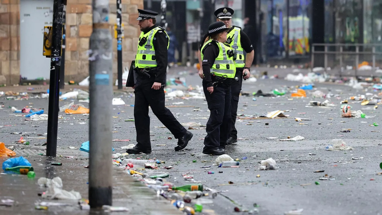  Police Scotland officers walk along a city street covered in litter and debris following large crowds gathering in Glasgow.