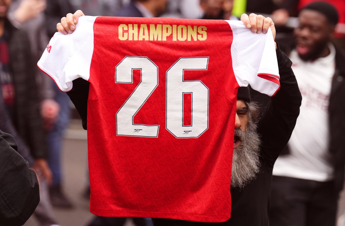 An Arsenal fan holding a 'Champions 26' shirt