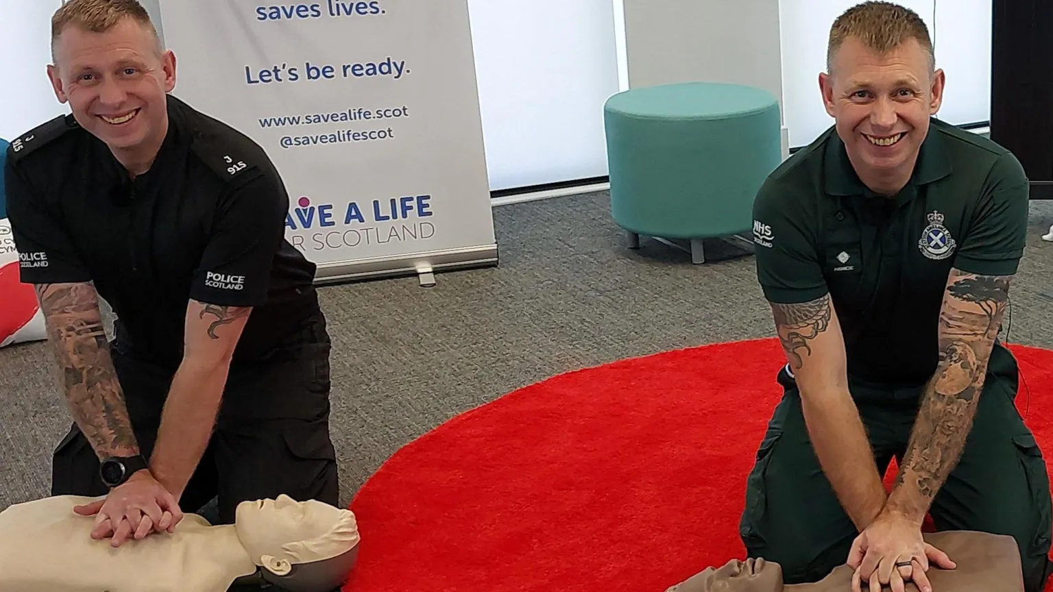 Scottish Ambulance Service Two men carry out CPR on dummy torsos, they are identical twins with short cropped hair but one is in a Police Scotland T-shirt and the other in a Scottish Ambulance Service one