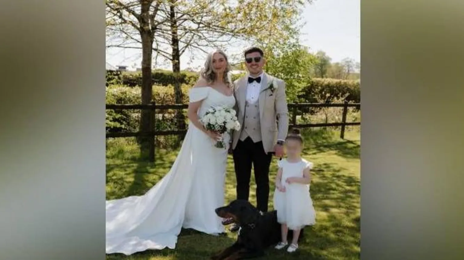 Kennedy News Ashleigh Stanley and Jake Stanley. She stand on the left in a wedding dress. He is on the right in black trousers, a beige jacket and waistcoat. Next to him is a small girl and a dobermann 