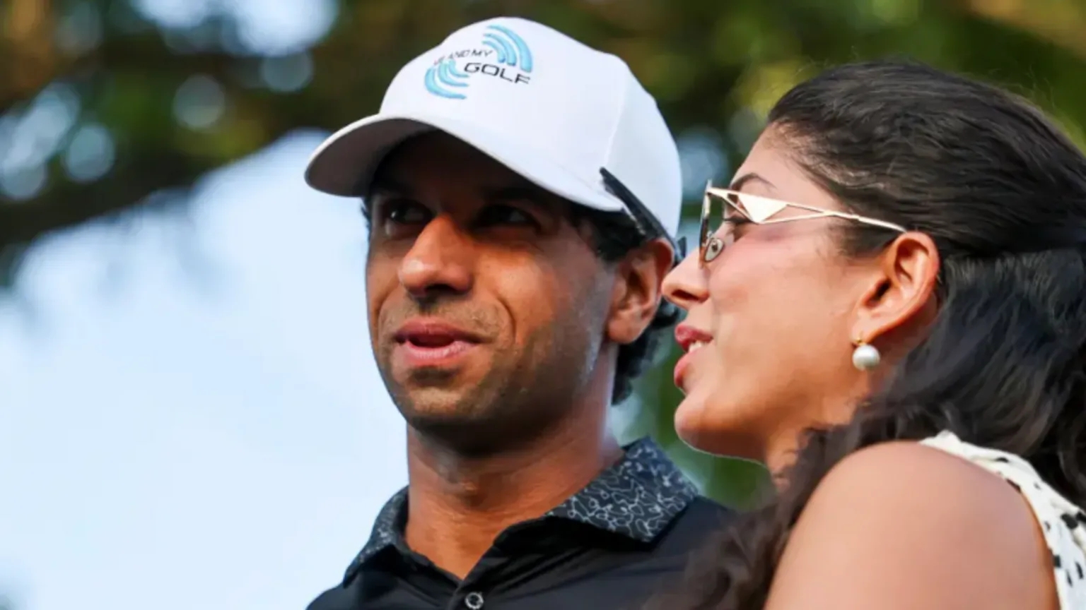  Rai is wearing a white cap and navy top and his wife had a summer blouse on with her hair tied back and sunglasses