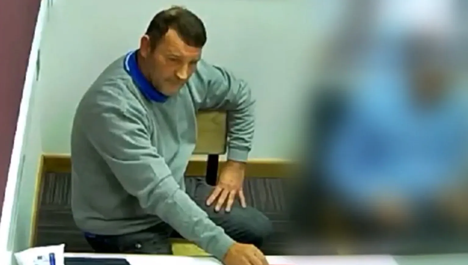 GMP Paul Quinn sat in a police interview room. Person sitting next to him is blurred. 