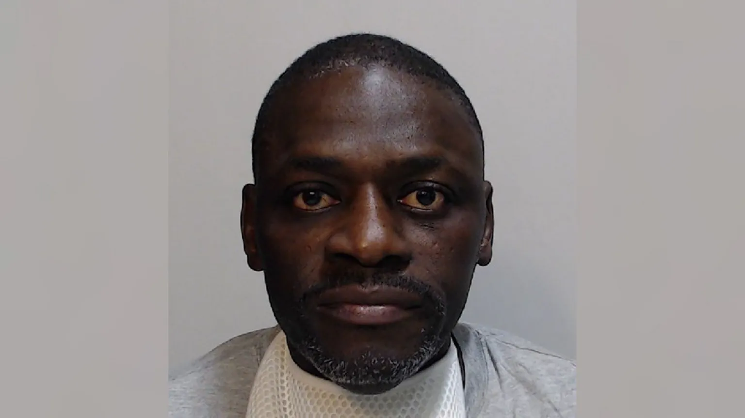 Police Scotland Momodou Bobb is staring at the camera. He is wearing a white T-shirt with a grey cotton top over it.